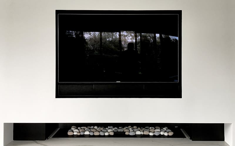 Large TV mounted above a fireplace in a white wall recess