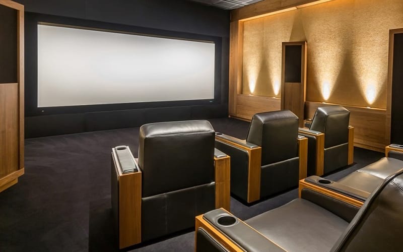 Home cinema room we built, with leather recliners facing a framed screen and lit timber panelling down one side
