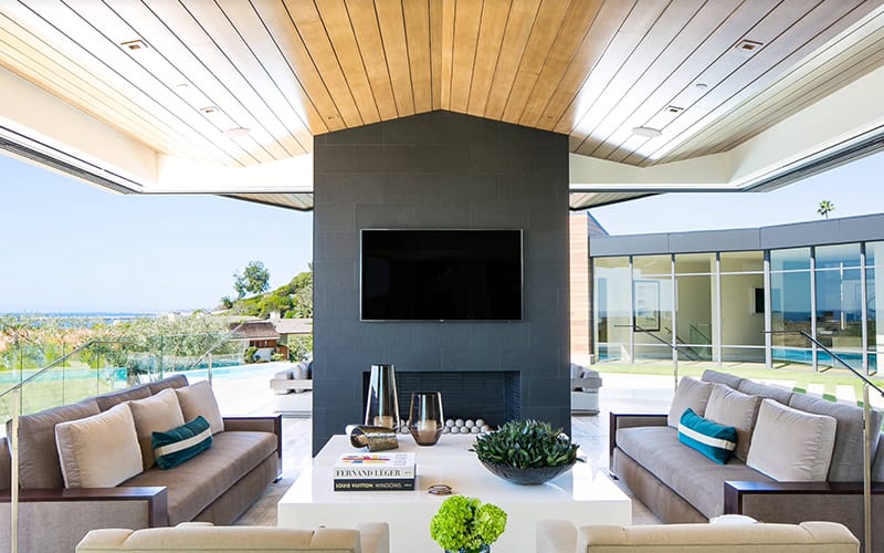 Outdoor entertaining area with a wall-mounted TV on a dark chimney breast overlooking a pool